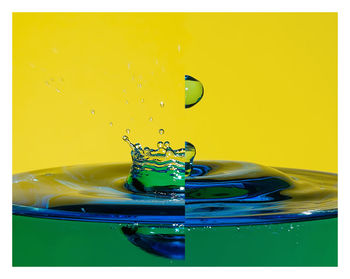 Close-up of drop splashing on water against yellow background