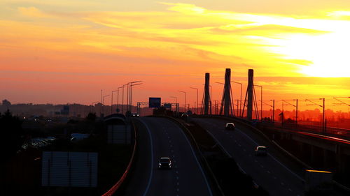 Cars moving on highway against sky during sunset