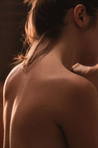 Midsection of shirtless young woman against black background