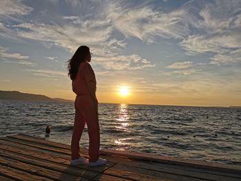 Woman standing at sea against sky during sunset