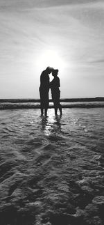 Silhouette friends standing on beach against sky