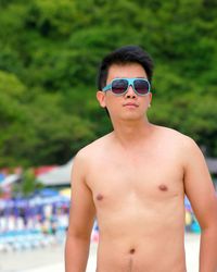 Portrait of shirtless man wearing sunglasses while standing at beach