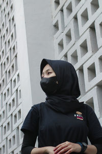 Portrait of young woman looking away while standing against wall