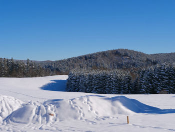 Snow covered field against clear blue sky