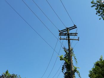 Low angle view of electricity pylon against clear blue sky