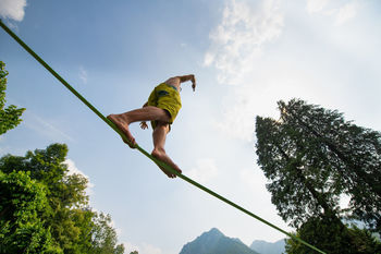 Low angle view of man walking on rope against sky
