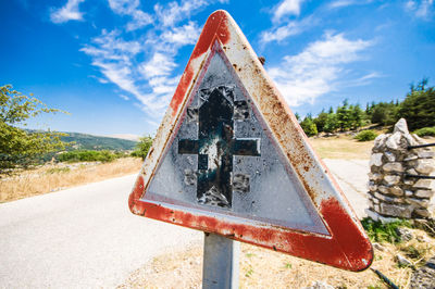 Close-up of rusty sign on road against sky