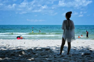 Rear view of woman standing at beach against sky