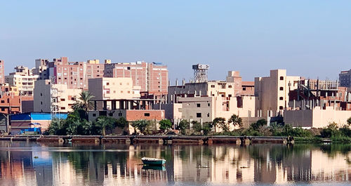 Buildings by river against clear blue sky