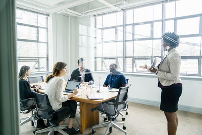 Businesswoman discussing with colleagues seen through window