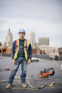 Portrait of male worker standing on building at construction site against cloudy sky