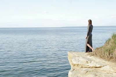 Woman standing on cliff by sea