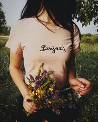 Midsection of woman holding flower while standing amidst plants on field