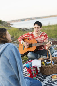 Man playing guitar for girlfriend while enjoying picnic on field