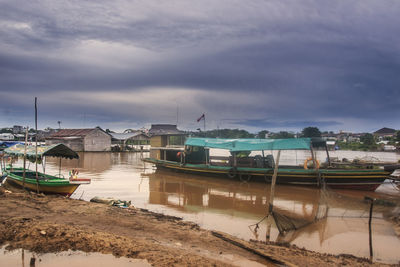 Boats moored at harbor against cloudy sky