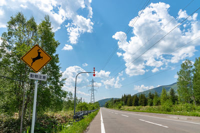 Road sign by trees against sky