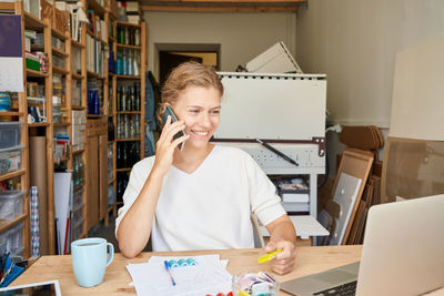 Smiling young woman using phone while sitting in office