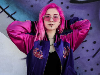 Portrait of young woman wearing sunglasses standing against wall