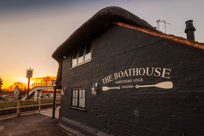 Information sign on street by building against sky during sunset