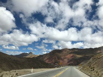 Empty road leading towards mountains against sky