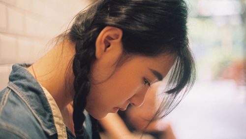 Side view of thoughtful young woman looking down while sitting at home