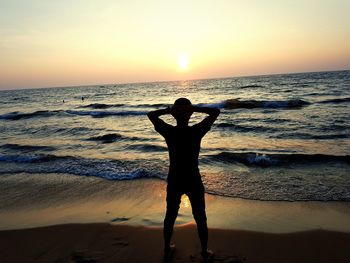 Silhouette man standing at beach against sky during sunset