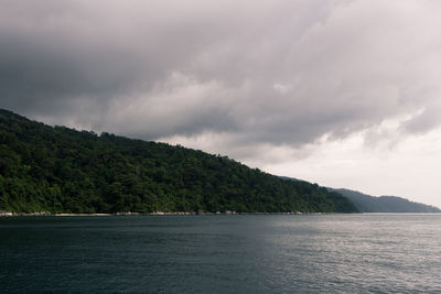 Scenic view of sea by mountain against sky