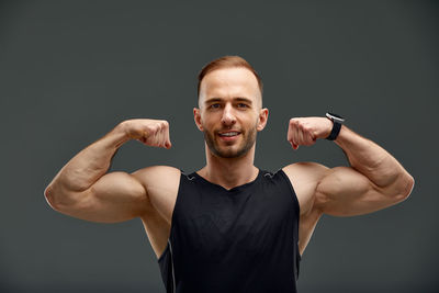 Portrait of young man flexing muscles against black background