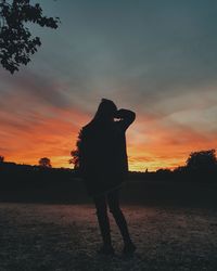 Silhouette woman standing on field against sky during sunset