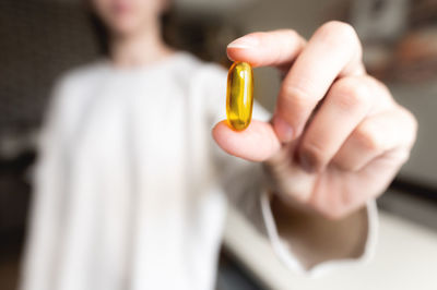 Woman's hand holds an omega-3 capsule against the background of herself in a white sweater, the
