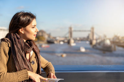 Young woman looking away against sky in city