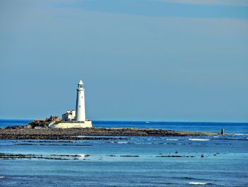 Lighthouse by sea against clear sky