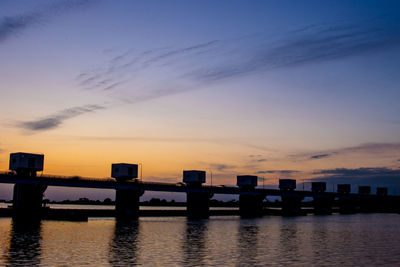 Pier over river against sky during sunset