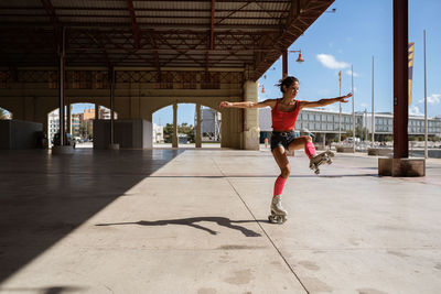 Concentrated female balancing on leg while roller skating on sports ground on sunny day in city