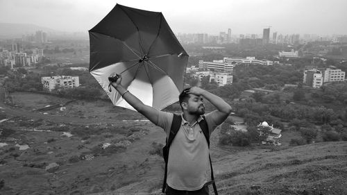 Woman with umbrella standing on city against sky