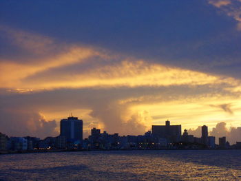 Sea by buildings against sky during sunset