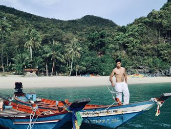 Full length of shirtless man standing on sea against mountain