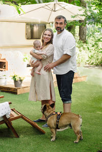 Family with baby and dog spending happy time together near trailer outside on deck chair, traveling