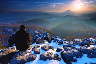 Man on rocks and looking at the snow-covered hills. dark sky with clouds.