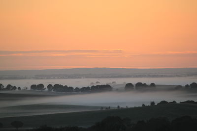 Scenic view of landscape in foggy weather against orange sky during sunset