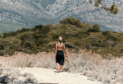 Rear view of young woman wearing summer clothes, walking on path through mediterranean landscape