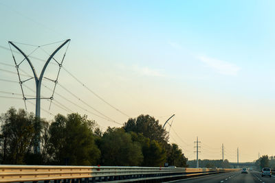 Road by trees against sky during sunset