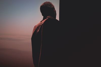 Rear view of man standing by sea against sky during sunset
