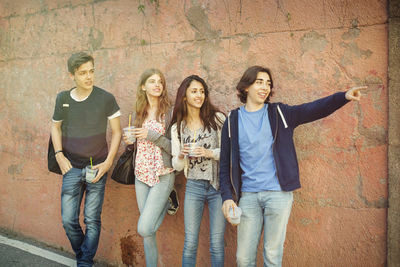 Happy teenager showing something to friends against wall