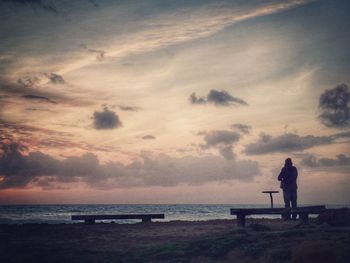 Silhouette man photographing sea against sky during sunset