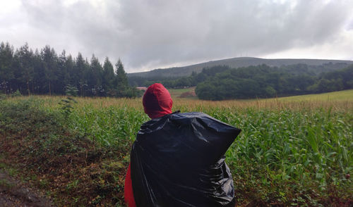 Rear view of person standing by plants on field against cloudy sky