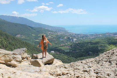 Full length of woman standing on rock against sky