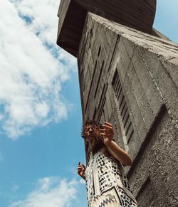 Low angle view of woman standing by concrete wall against sky