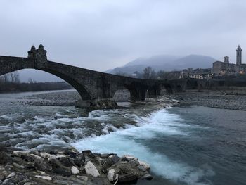 Arch bridge over river against sky, bobbio italy 