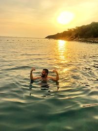 Man swimming in sea against sky during sunset